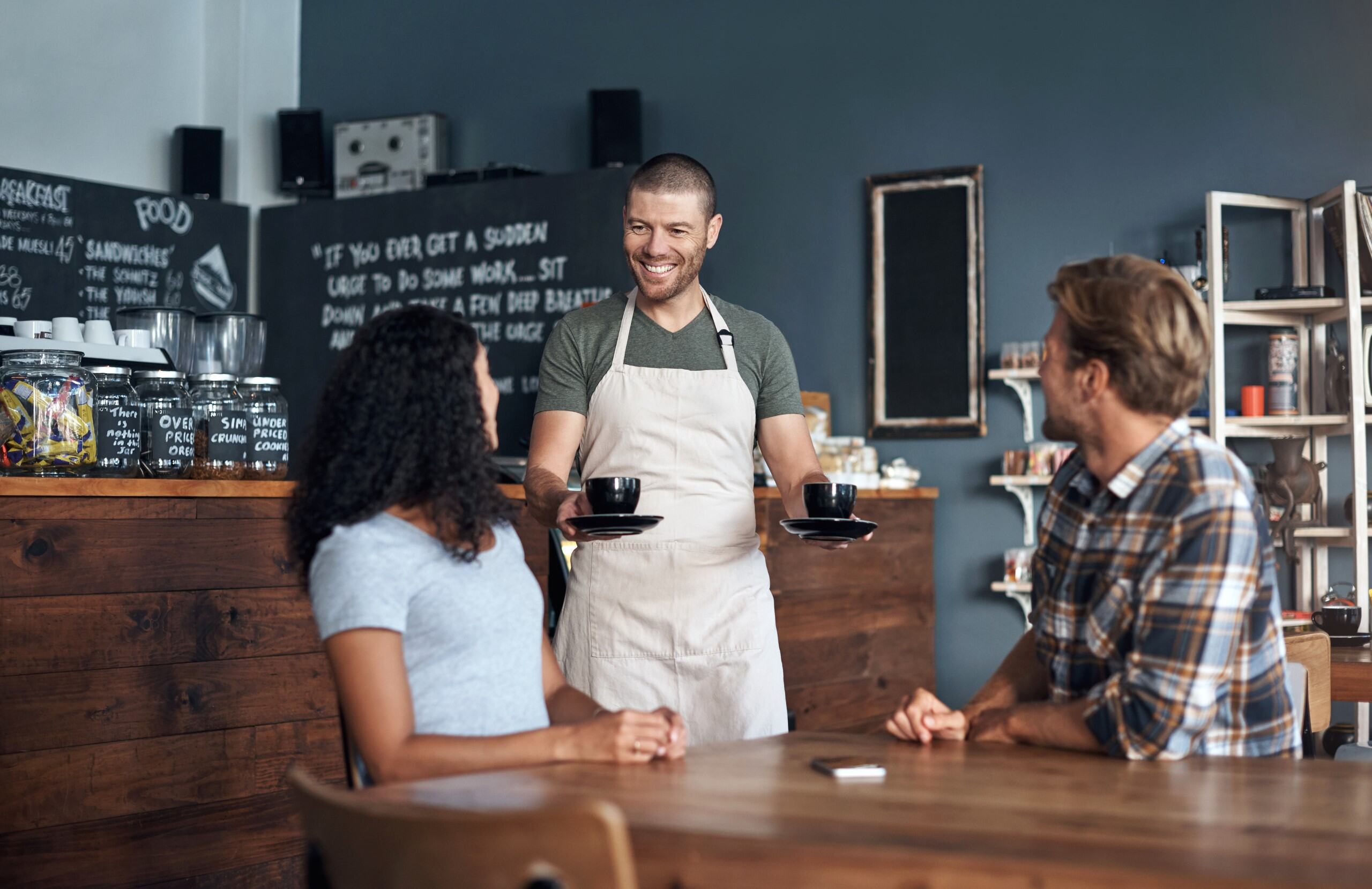 Cafe worker serves two hot beverages to patrons.
