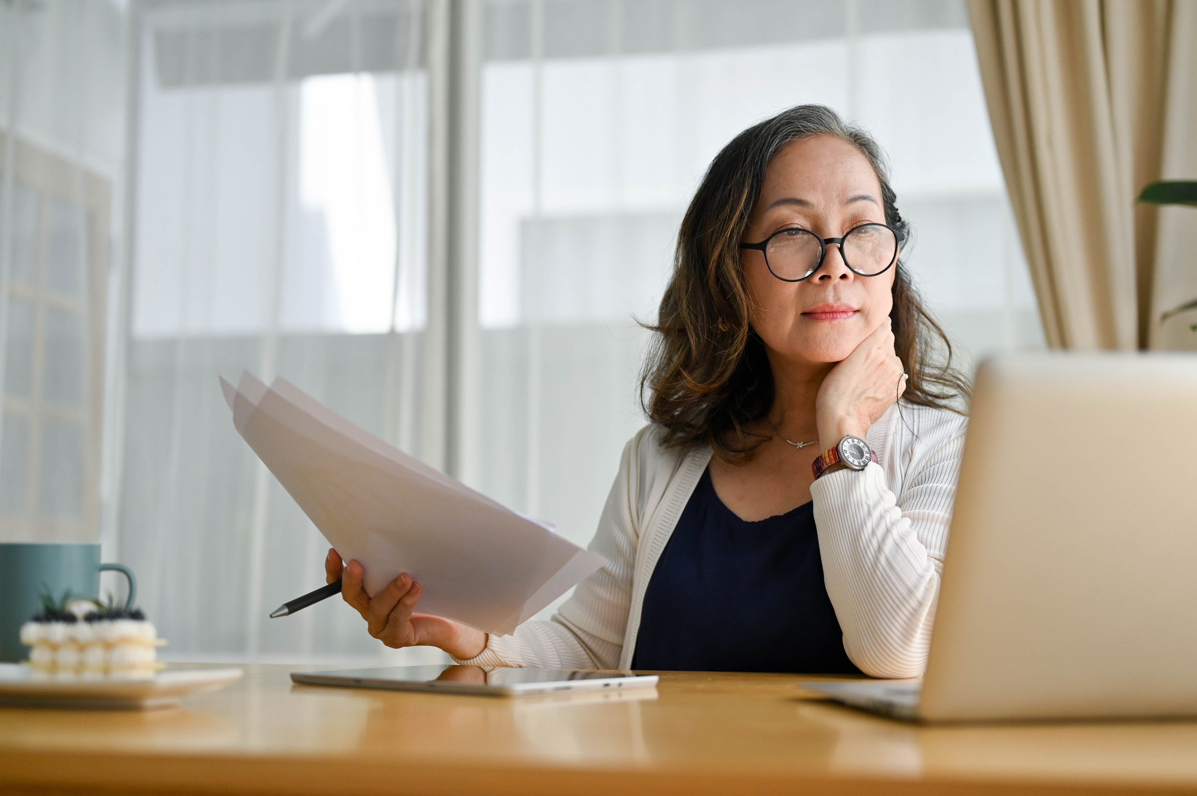 Woman holds a printout and looks at a screen.