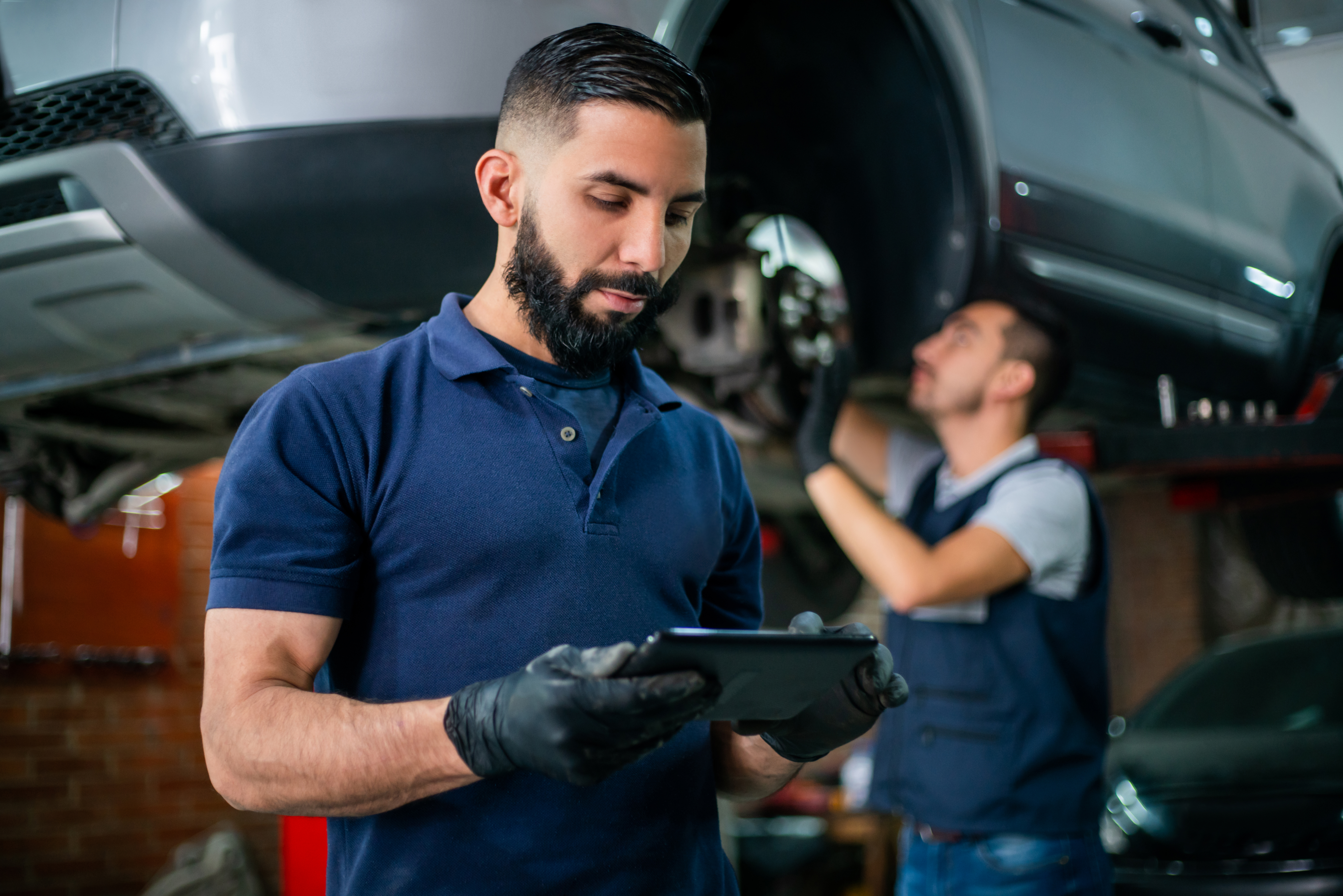 Auto repair worker stands in front of lifted car