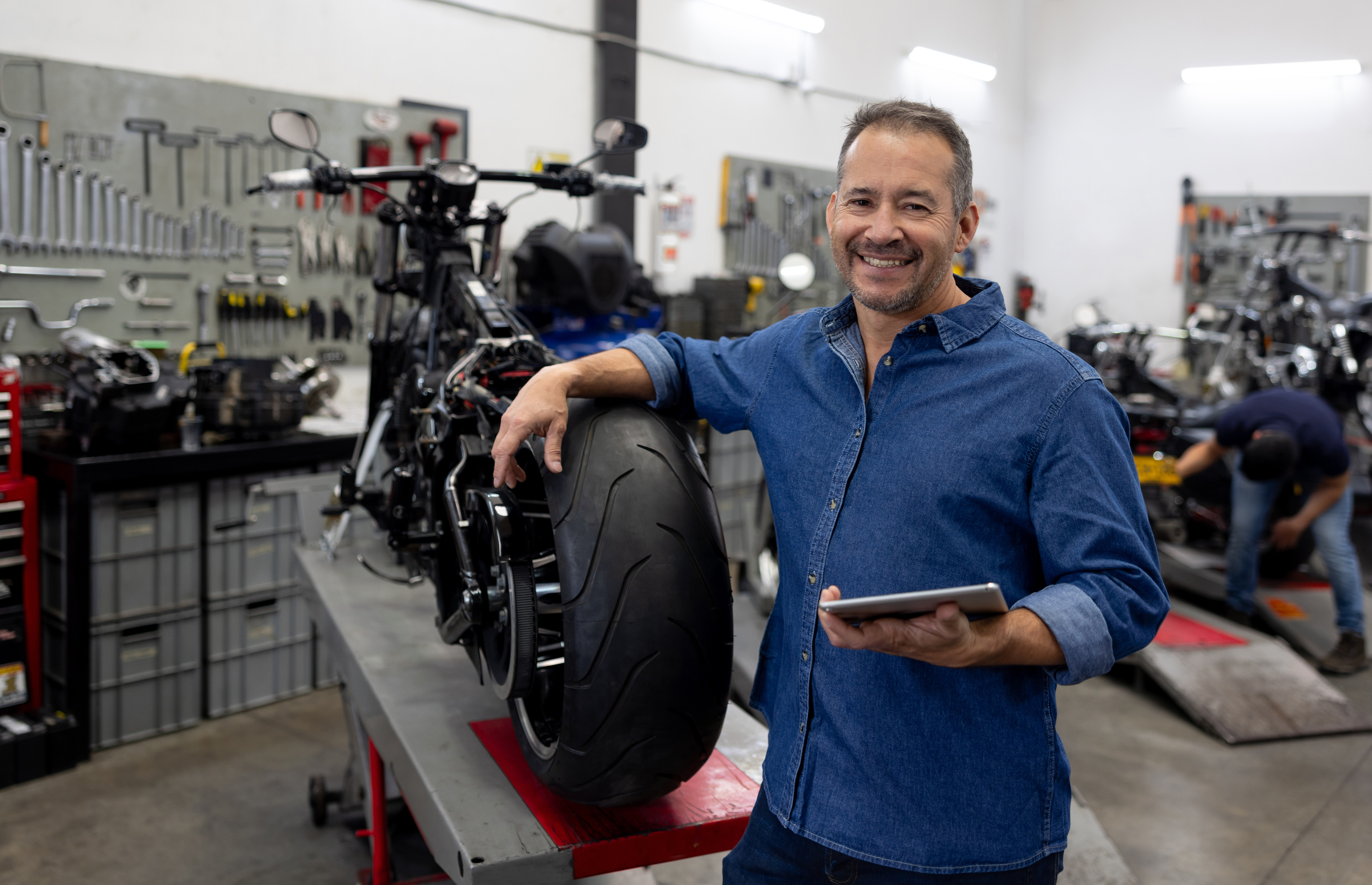 Garage worker rests his arm on the back wheel of a motorcycle.