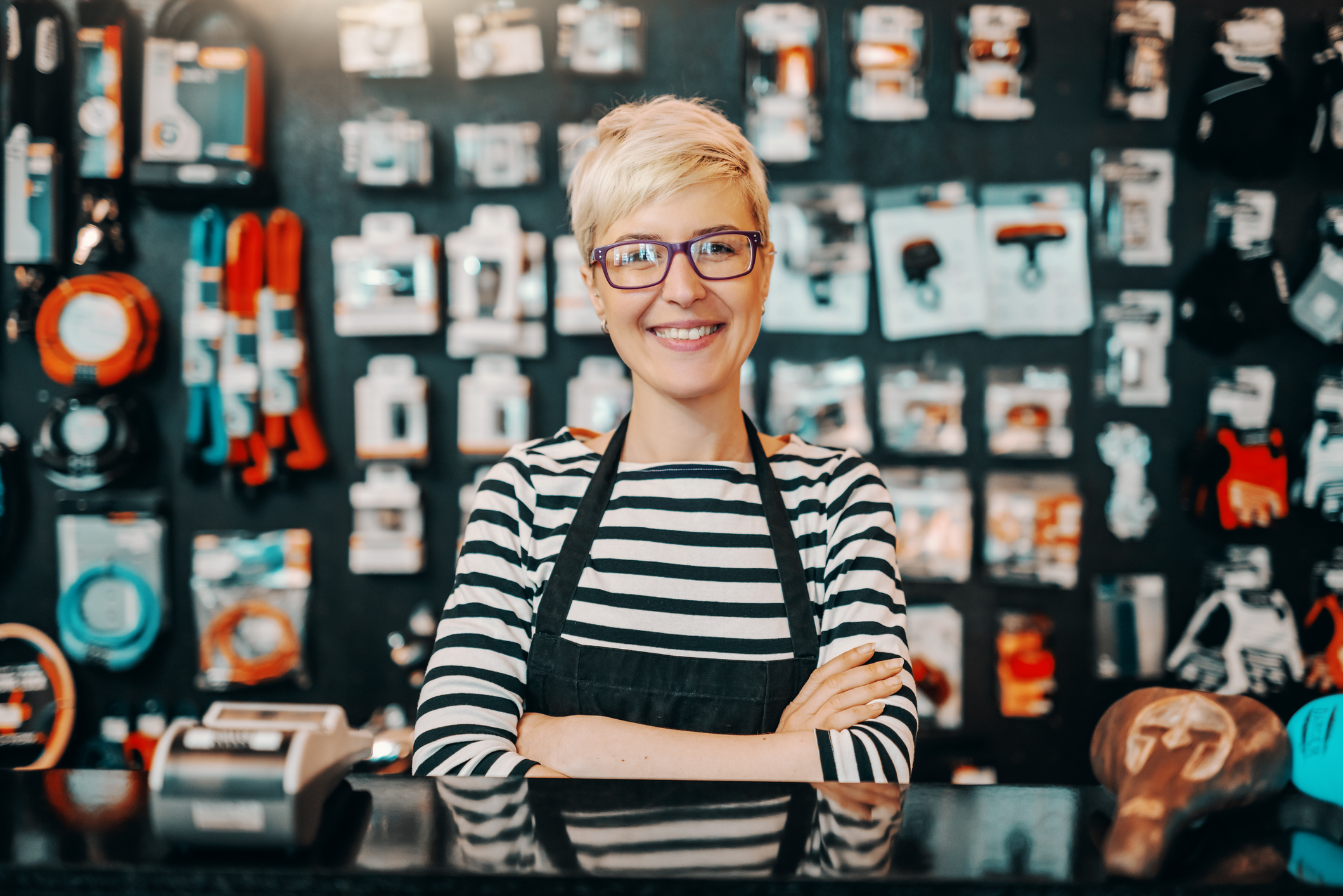 Smiling female worker with short blonde hair standing in bicycle shop with arms crossed
