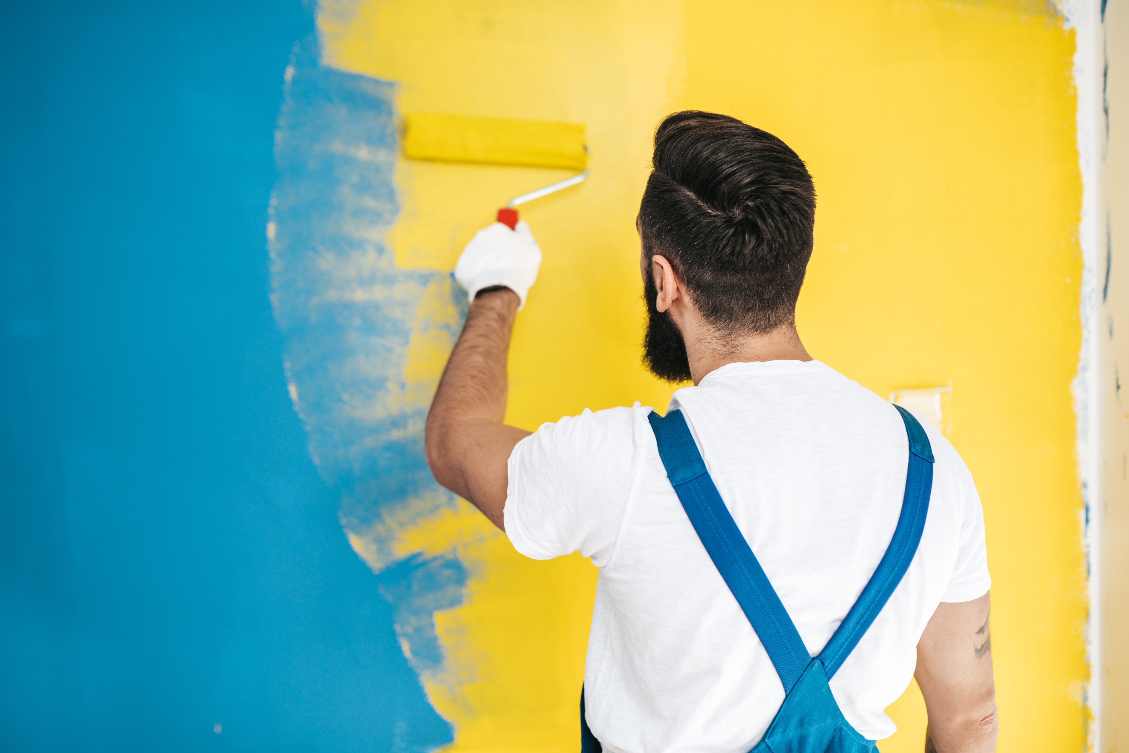 Man painting a wall in blue or teal and yellow colors