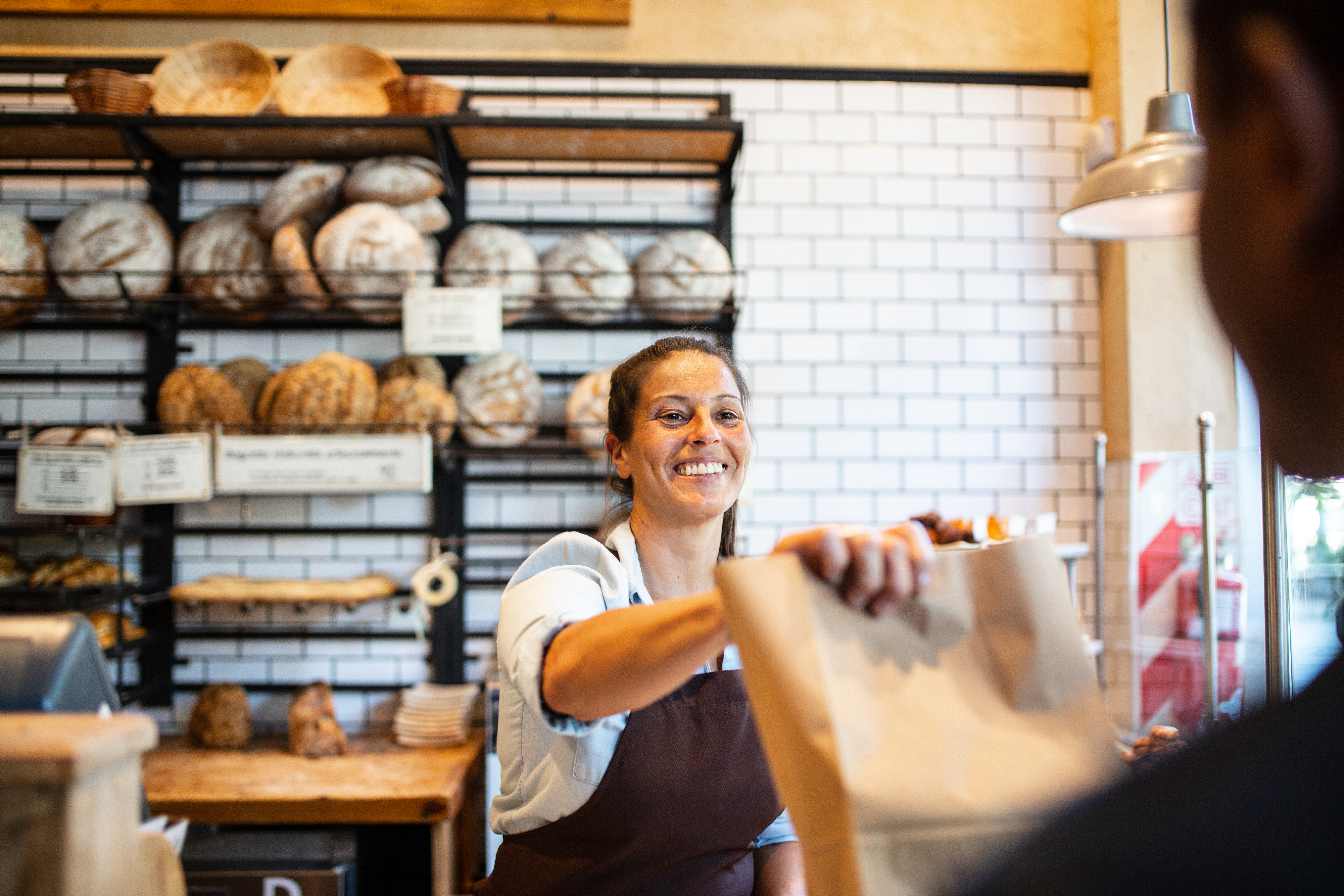 Bakery owner hands baked goods to customer across counter